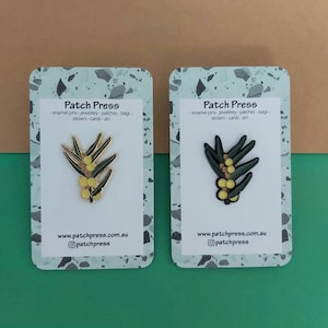 Könnte beinhalten: Zwei weiße Karten mit einem grünen und schwarzen Terrazzo-Muster als Rand. Jede Karte zeigt eine goldene Emaille-Anstecknadel mit einem Mimosenzweig mit gelben Blüten. Der Text auf den Karten lautet "Patch Press - Emaille-Anstecknadeln - Schmuck - Patches - Taschen - Aufkleber - Karten - Kunst - www.patchpress.com.au @patchpress"