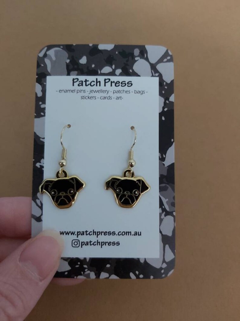 Puede incluir: Pendientes de aro dorados con caras de carlino de esmalte negro. Los pendientes est&aacute;n en una tarjeta blanca con el texto "Patch Press" y "www.patchpress.com.au" y "@patchpress".
