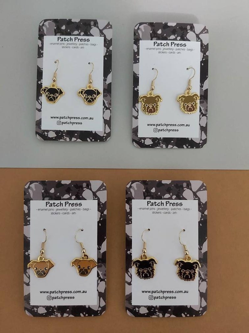 Puede incluir: Cuatro pares de pendientes de tono dorado con abalorios de perro pug negro y marr&oacute;n. Los pendientes se muestran en tarjetas blancas con dise&ntilde;os de pintura salpicada en blanco y negro. Las tarjetas tienen el texto "Patch Press" y la direcci&oacute;n del sitio web "www.patchpress.com.au".