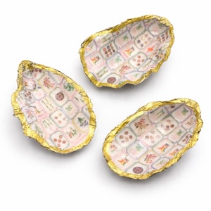 May include: Three decorative oyster shell dishes with gold leaf edges. The interior of each shell features a patterned design with various colorful motifs. The shells are arranged on a white background.