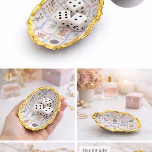 May include: An oval-shaped trinket dish with a gold leaf rim and a white interior featuring a grid of small floral patterns. Three white six-sided dice with black pips are placed inside the dish. The dish has an irregular, textured edge.