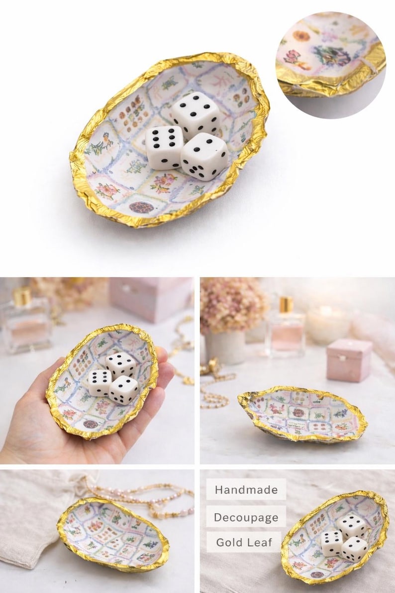 May include: An oval-shaped trinket dish with a gold leaf rim and a white interior featuring a grid of small floral patterns. Three white six-sided dice with black pips are placed inside the dish. The dish has an irregular, textured edge.