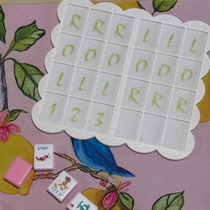 May include: A white game board with a scalloped edge, featuring a grid of squares with the letters R, O, and L, and numbers 1, 2, and 3. Several Mahjong tiles with pink edges and various symbols are scattered around the board.