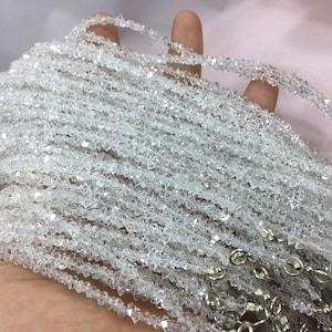 May include: A collection of clear, faceted crystal beads strung together to form multiple strands. The beads are small and irregular in shape, with a sparkling, translucent appearance. The strands are held together with silver-colored clasps.