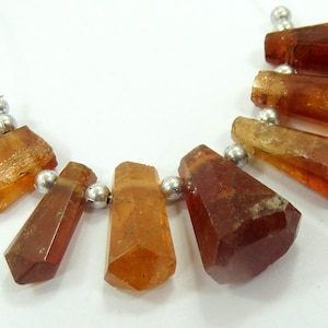 May include: A strand of faceted, amber-colored gemstone beads. The beads are strung on a thin, clear cord with small, silver-colored metal beads between each gemstone. The gemstones have a variety of shapes.