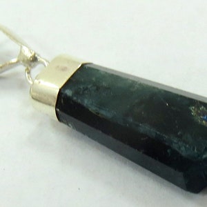 May include: A dark green, hexagonal gemstone pendant with a silver-colored bail. The gemstone has a polished, faceted surface and a metallic silver cap. The pendant is likely a piece of jewelry.