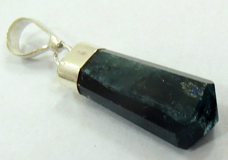 May include: A dark green, hexagonal gemstone pendant with a silver-colored bail. The gemstone has a polished, faceted surface and a metallic silver cap. The pendant is likely a piece of jewelry.