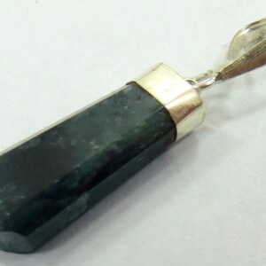 May include: A dark green, hexagonal pendant with a silver-colored bail. The gemstone has a polished, faceted surface and is set with a silver-colored metal cap. The pendant is a simple, elegant piece of jewelry.