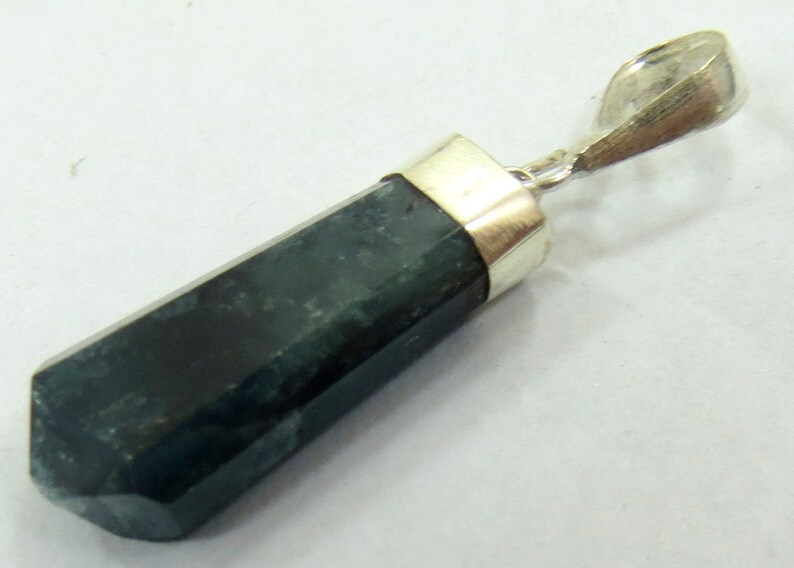May include: A dark green, hexagonal pendant with a silver-colored bail. The gemstone has a polished, faceted surface and is set with a silver-colored metal cap. The pendant is a simple, elegant piece of jewelry.