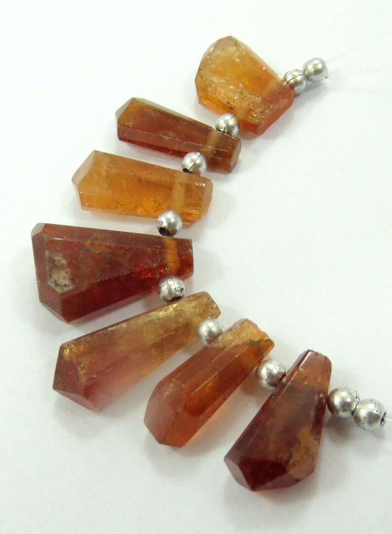 May include: A strand of faceted, amber-colored gemstone beads with silver-colored spacer beads. The gemstones have a natural, crystalline appearance and vary in size and shape. The beads are strung on a clear, thin cord, suitable for jewelry making.