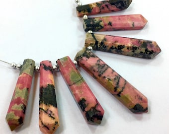 Könnte beinhalten: Eine Sammlung länglicher Edelsteinperlen mit facettierten Oberflächen. Die Perlen sind überwiegend rosa mit grünen und schwarzen Adern. Jede Perle ist auf einem dünnen Silberdraht mit kleinen Silberperlen aufgefädelt. Die Edelsteine sind vor weißem Hintergrund.
