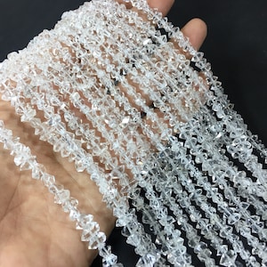 May include: Strands of clear, faceted quartz beads. The beads are irregularly shaped, with multiple facets catching the light. The quartz beads are strung together, creating a shimmering effect. The beads are held in a hand.