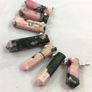 May include: Pink and black gemstone pendants with silver beads strung on a white thread. The pendants are hexagonal in shape and vary in the amount of pink and black color. The gemstones are likely used for jewelry making.