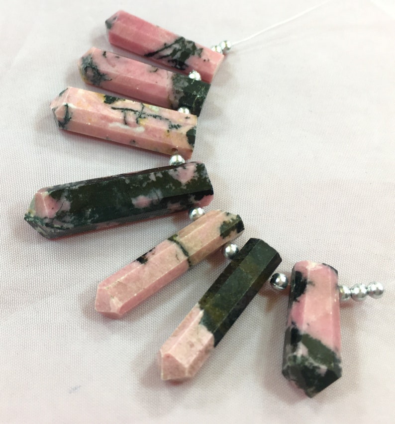 May include: Pink and black gemstone pendants with silver beads strung on a white thread. The pendants are hexagonal in shape and vary in the amount of pink and black color. The gemstones are likely used for jewelry making.