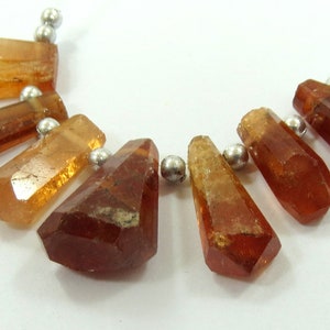 May include: A necklace featuring faceted, amber-colored gemstone beads. The beads are strung on a silver-colored wire, with small silver beads separating each gemstone. The gemstones have a geometric, crystal-like shape.