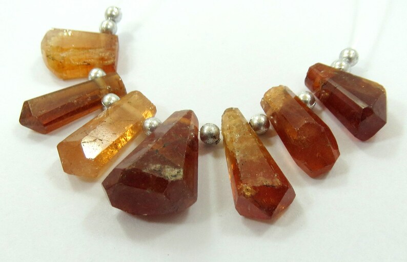 May include: A necklace featuring faceted, amber-colored gemstone beads. The beads are strung on a silver-colored wire, with small silver beads separating each gemstone. The gemstones have a geometric, crystal-like shape.