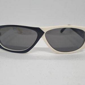 Könnte beinhalten: Eine Sonnenbrille in Schwarz und Weiß mit einem geometrischen Rahmen. Die Sonnenbrille hat dunkle Gläser.