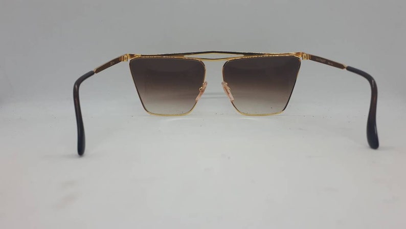 Pu&ograve; includere: Occhiali da sole dorati con lenti marroni sfumate e aste nere.