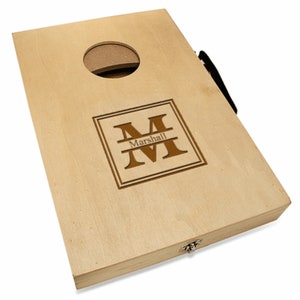 May include: A wooden cornhole game with a personalized monogram and the name "Marshall" engraved on the front. The game is closed and has a black handle.