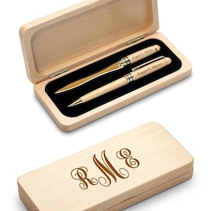 May include: A wooden pen and letter opener set in a light-colored wooden box. The pen and letter opener are light-colored with silver accents. The box is open, revealing the items inside, and the closed box has the initials "R M E" in a decorative font.