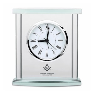 May include: A glass clock with a white face and black Roman numeral hour markers. The clock has a silver frame and a silver base. The clock is engraved with a Masonic symbol and the text "Honorable Donald Clay Ashley Lodge #232".