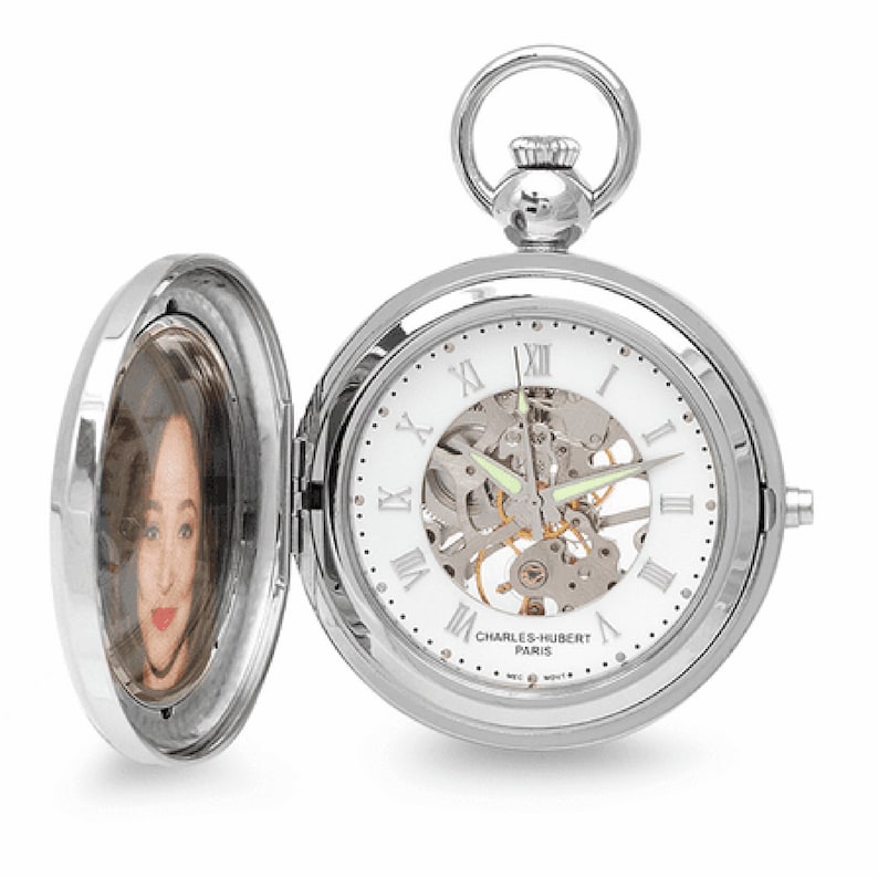 May include: A silver pocket watch with a white face and Roman numeral hour markers. The watch has a skeletonized movement and a photo insert on the back.