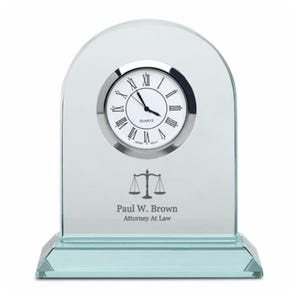 May include: A glass desk clock with a silver face and Roman numeral hour markers. The clock has a scale of justice symbol and the text "Paul W. Brown Attorney At Law" engraved on the base.