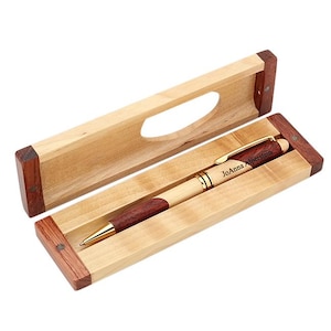 May include: A wooden pen and box set with a personalized inscription that reads "JoAnna Alperstein". The pen has a gold trim and a red and brown wood design. The box is made of light wood with a dark wood trim.