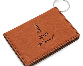 May include: A brown leather key chain with a metal ring. The keychain has the initial "J" and the name "JOHN Kennedy" engraved on it.