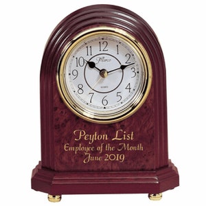 May include: A mahogany wood desk clock with a gold trim around the face. The clock face has white numbers and hands. The clock has a personalized inscription that reads "Peyton List Employee of the Month June 2019".