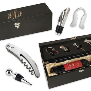 May include: A black wooden wine box with a gold engraved monogram "S.K.F." and a silver wine opener, bottle stopper, and pourer. The box also includes a bottle of red wine.