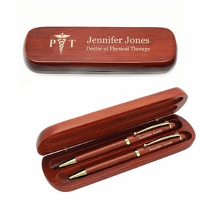 May include: A wooden pen and pencil set in a mahogany case with a gold-toned medical symbol and the text "PT" engraved on the top. The case is engraved with the name "Jennifer Jones" and the title "Doctor of Physical Therapy".
