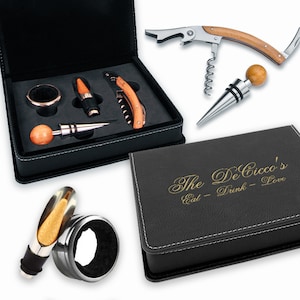 May include: A black leatherette gift box with a gold inscription that reads "The De Cicco's Eat - Drink - Love". The box contains a wine opener, a bottle stopper, and a ring pull.