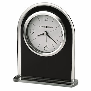 May include: A black and silver alarm clock with a white face and black hands. The clock has a silver frame and a black base. The clock face has the words "Howard Miller" printed on it.