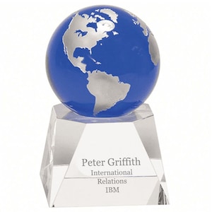 May include: A blue glass globe with a silver world map sits on a clear crystal base. The base is engraved with the text "Peter Griffith, International Relations, IBM."