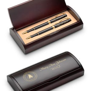 May include: A dark brown wooden pen set with two black pens with gold accents, presented in an open box. The pens and box lid are engraved with the name "Mary Ann Johnson" and "USSF". The box also features a gold emblem.