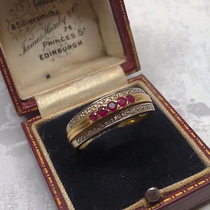 以下が含まれることがあります： 赤い宝石がバンドにセットされた金と銀のリング。リングは「Goldsmiths＆Silversmiths James Hardy 74 Princes St Edinburgh」という刻印がされた赤いベルベットの箱に入っています。