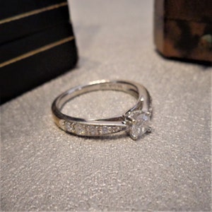Op de afbeelding: Een zilveren verlovingsring met een enkele ronde diamant en een band met kleinere diamanten.