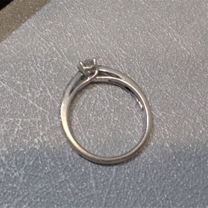 Op de afbeelding: Een zilveren ring met een kleine, heldere edelsteen in een kraalbezetting. De band is dun en heeft een rij kleine, heldere edelstenen.