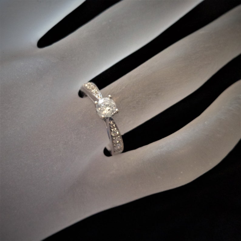 Op de afbeelding: Een zilveren verlovingsring met een enkele ronde diamant in het midden en kleinere diamanten die in een band zijn gezet.