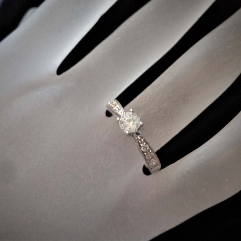 Op de afbeelding: Een zilveren verlovingsring met een enkele ronde diamant en kleinere diamanten die in de band zijn gezet.