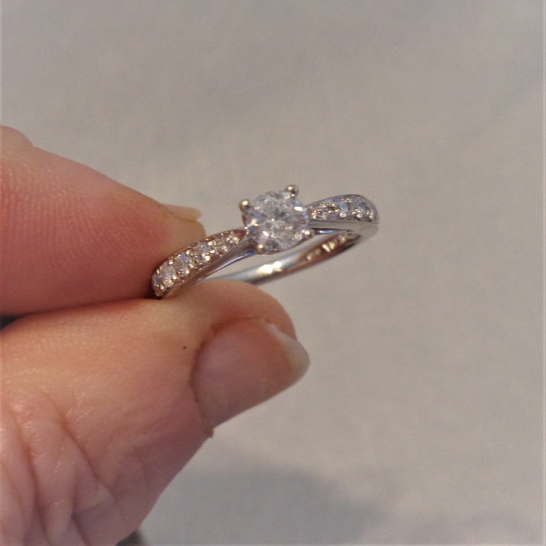 Op de afbeelding: Een zilveren verlovingsring met een ronde centrale diamant en kleinere diamanten die in een pav&eacute;-setting op de band zijn gezet.