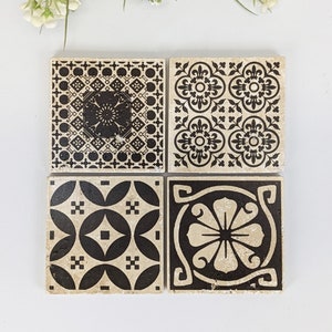 Könnte beinhalten: Vier quadratische Keramikuntersetzer mit schwarz-weißen geometrischen Mustern. Jeder Untersetzer hat ein einzigartiges Design, darunter Blumen- und abstrakte Motive. Die Untersetzer sind quadratisch angeordnet.