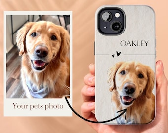 Op de afbeelding: Een witte telefoonhoes met een bruine, textuurrijke achtergrond. De hoes heeft een uitsparing voor de cameralens en een zwarte lijn met twee kleine hartjes boven de tekst "OAKLEY". Een golden retriever hond is afgebeeld op de hoes.