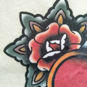 May include: A close-up of a traditional tattoo design featuring a red rose with green and black leaves. The rose is surrounded by a yellow and orange circle.