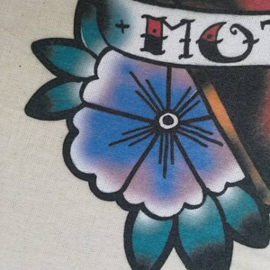 May include: A traditional tattoo design featuring a red heart with a banner that reads "MOM". The heart is surrounded by a blue flower with a white center and teal leaves.