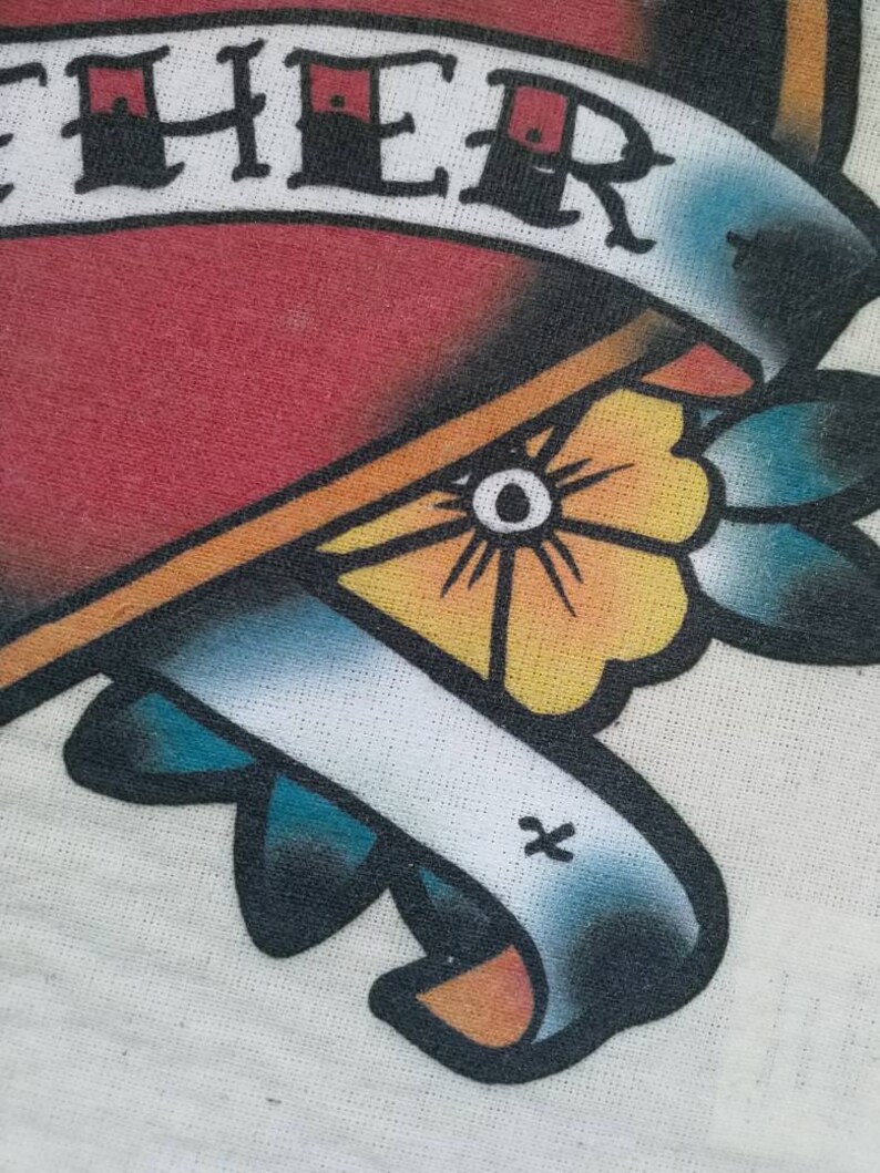 May include: A white t-shirt with a red heart and a banner that says "Together". The heart is outlined in black and has a yellow flower with a blue center. The banner is blue and white with a yellow outline.