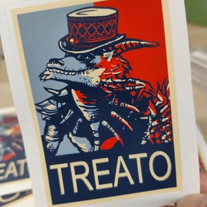 May include: A playing card featuring a stylized illustration of a creature wearing a top hat. The design uses red, blue, and white colors. The word "TREATO" is printed in large white letters at the bottom of the card.