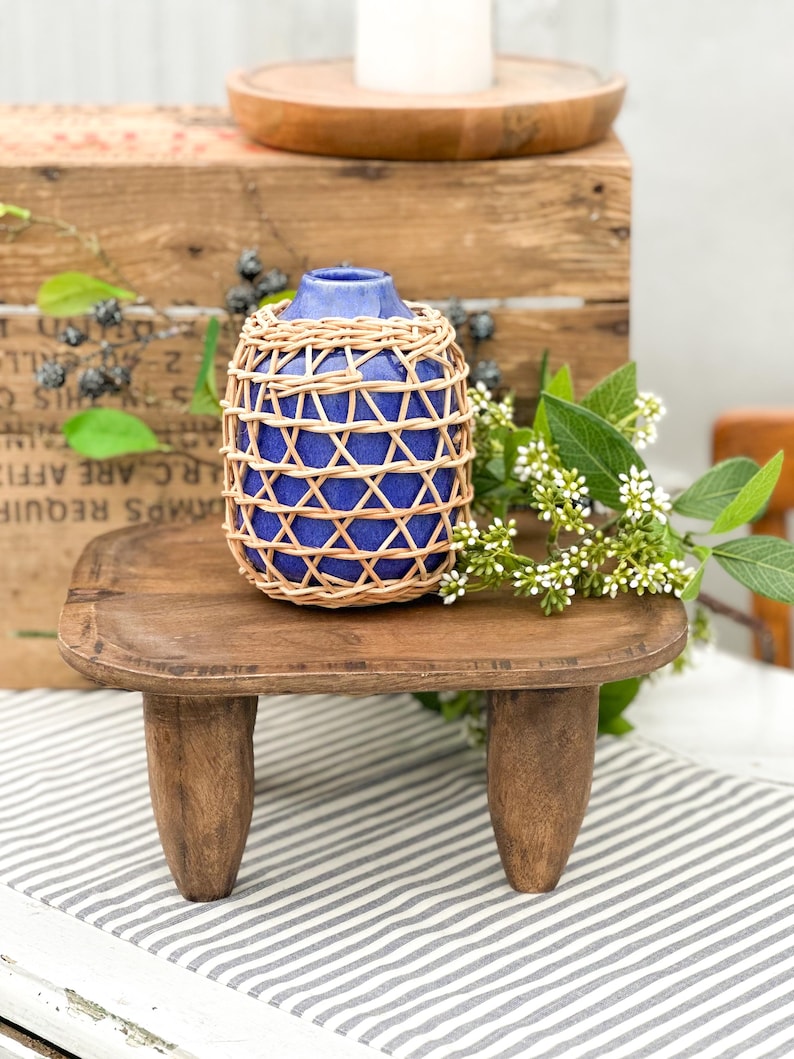 May include: A small, cobalt blue ceramic vase encased in a decorative, light-colored woven rattan lattice. The vase has a rounded body and a narrow neck, featuring a smooth, glossy finish that contrasts with the textured, natural fiber overlay.