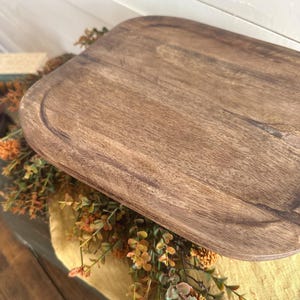 May include: A rectangular wooden serving tray with rounded corners and a smooth, dark brown grain finish. The tray features a shallow recessed surface with a defined border edge, showcasing natural wood textures and variations in color.